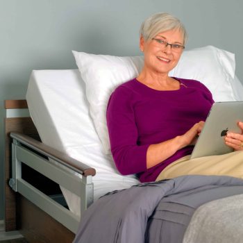 a woman sitting on a bed holding a tablet.