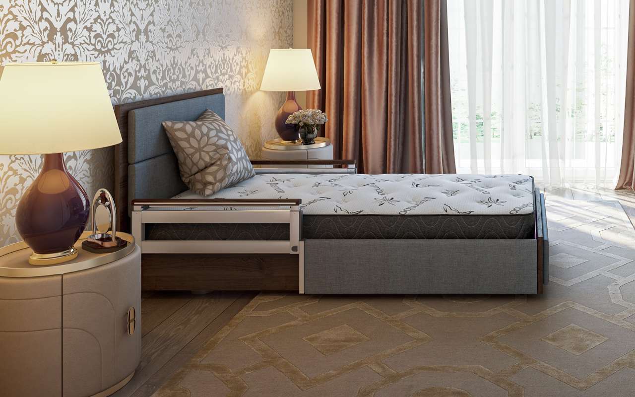 A neatly made bed next to two bedside tables with lamps, set in a room with patterned wallpaper, a carpeted floor, and sheer curtains allowing natural light into the room.