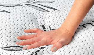 A person’s hand pressing down on a white, patterned mattress, testing its firmness.