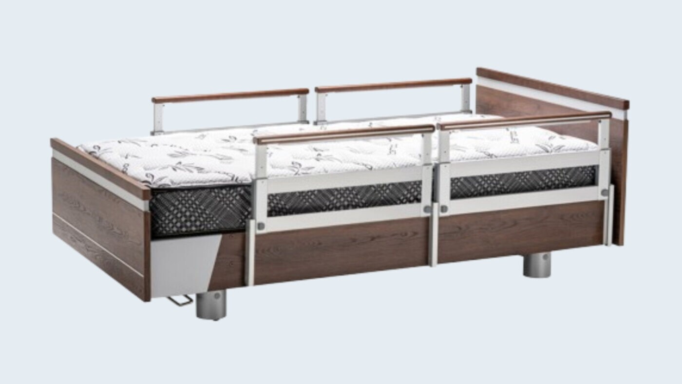 A hospital bed with a white and black patterned mattress, featuring wooden side panels and metal rails.