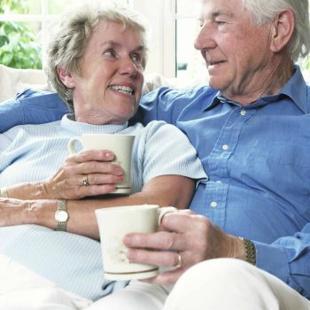 a man and woman sitting on a couch holding a cup of coffee.