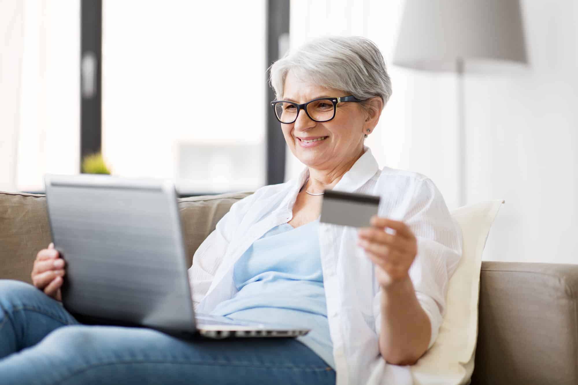 A woman utilizing a laptop while making an online purchase with her credit card from the comfort of an electric adjustable bed, highlighting its health advantages for seniors.