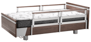 Hospital bed featuring PR39 side rails, a sturdy wood and metal frame, and a mattress with a patterned cover.