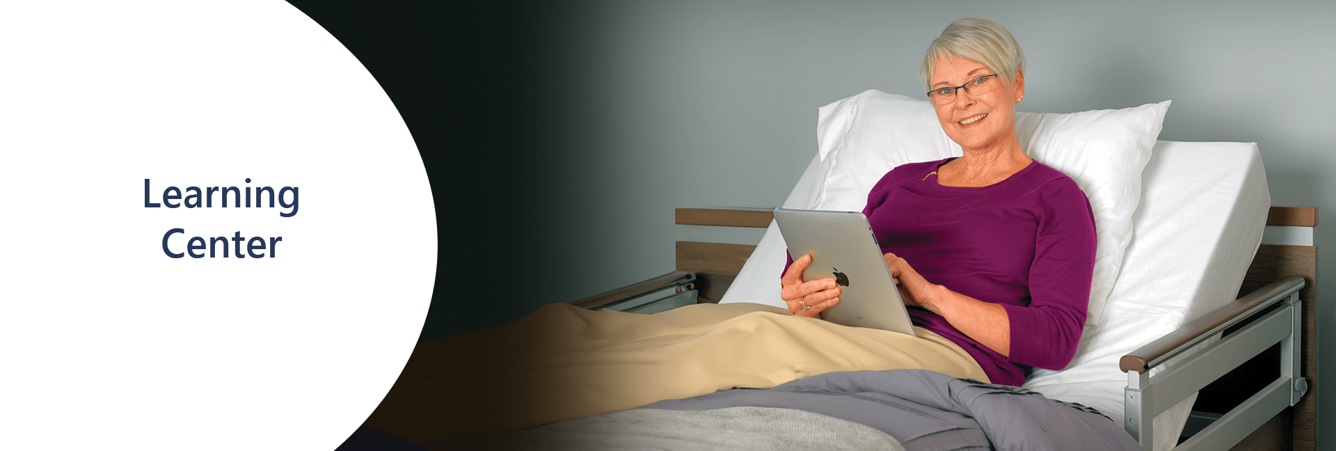 A smiling woman with short gray hair, wearing glasses and a purple top, reclines in a bed while using a tablet. The text "Learning Centre" appears on a white background to the left, emphasizing the focus on education.