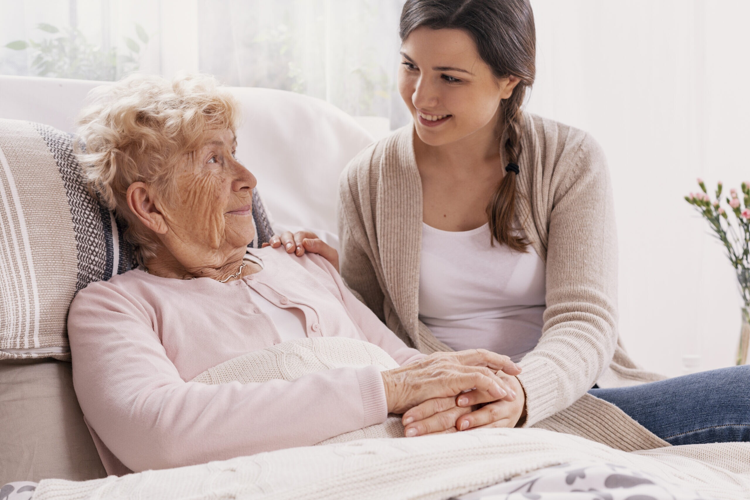 A woman is sitting on a bed with an elderly woman.