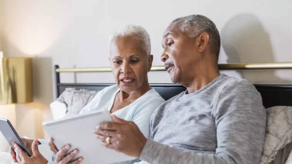 An older couple looking at a tablet computer in bed.