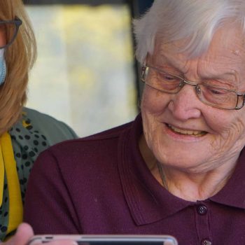 an older woman wearing a face mask looking at a cell phone.