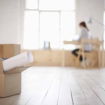 a woman sitting at a table in a room with boxes on the floor.