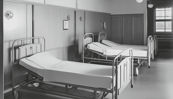 A hospital room with three empty beds, each equipped with white sheets and metal frames. The room has wooden panel walls, a window allowing natural light, and makes one ponder: Are home hospital beds as comfortable as a normal bed?