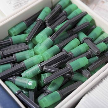 a box filled with lots of green and black markers. a box filled with lots of green and black markers.